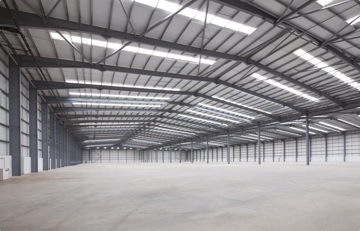 Inside the warehouse: a clear-span steel portal frame over a wide, empty concrete floor, lit by roof lights